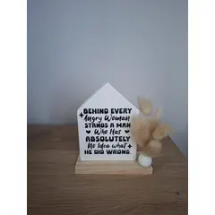 Pločica od gipsa u obliku kućice  sa šaljivim natpisom i suhim cvijećem na drvenom postolju.